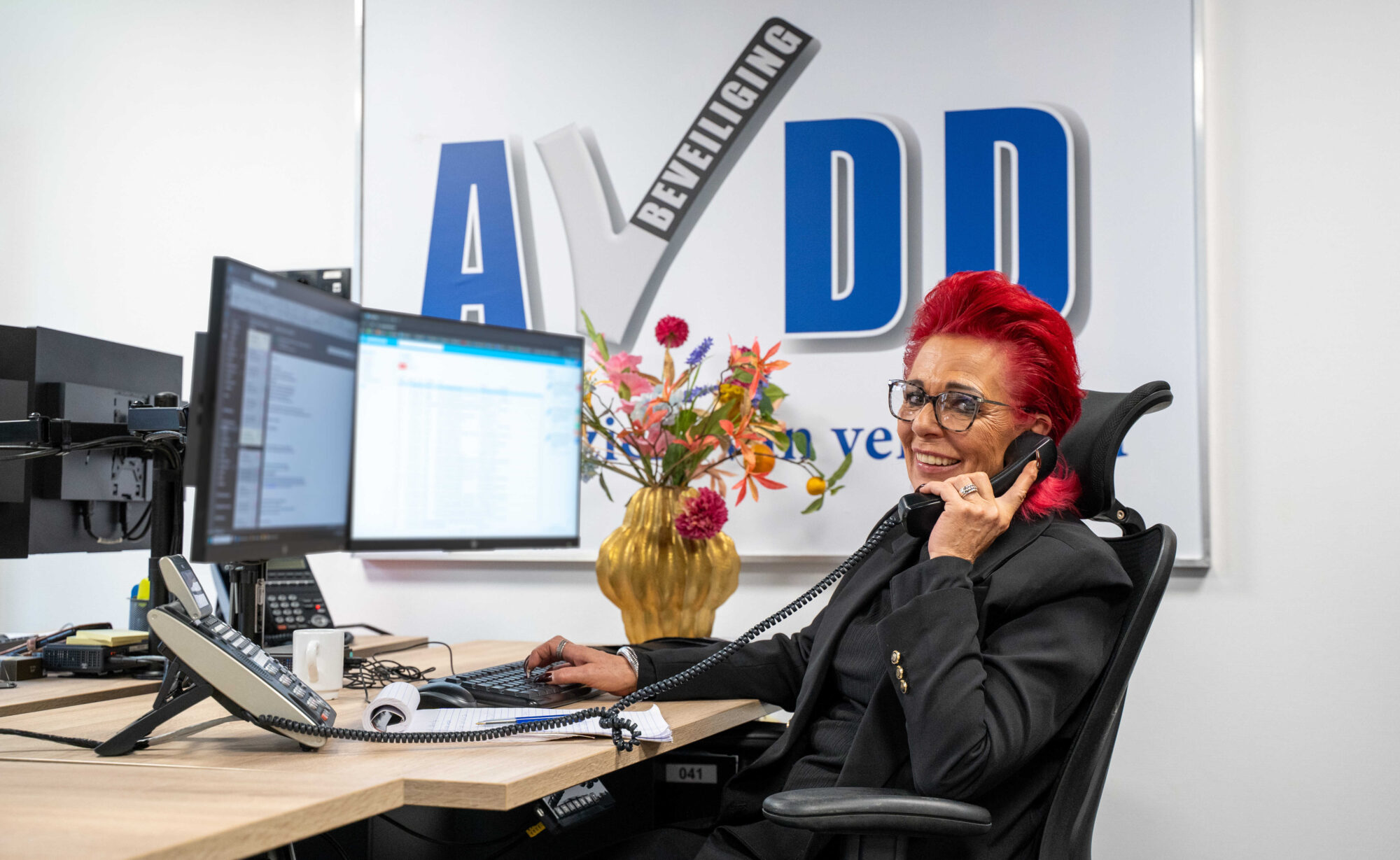 Medewerker vrouw van AVDD Beveiliging achter haar bureau aan de telefoon namens beveiligingsbedrijf